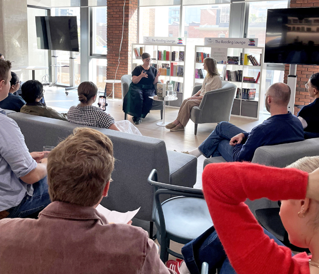Two women seated on armchairs at the front, while an audience listens to the discussion.