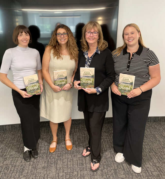 Four women stand together, each holding a copy of the novel Finding Flora