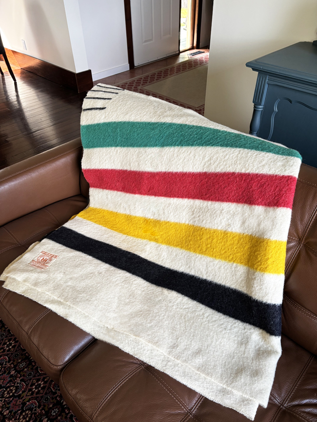 Striped green, red, yellow and black Hudson Bay trading blanket tossed over the back of a couch.