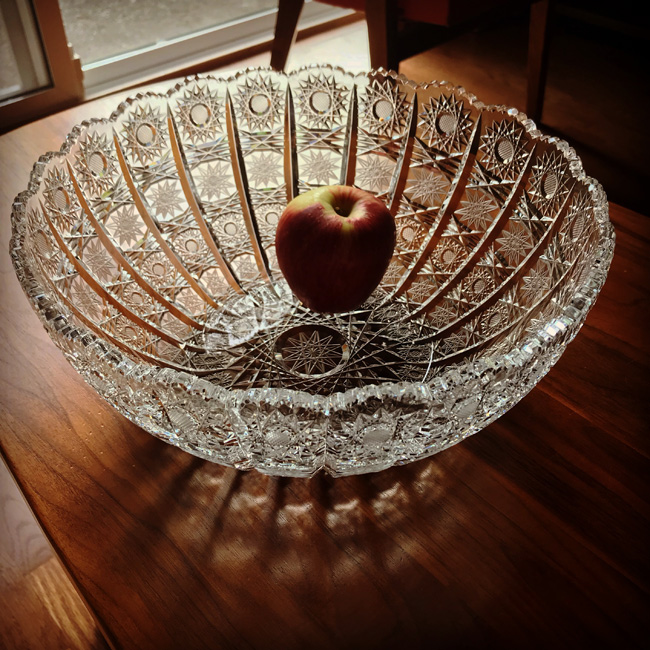 Crystal salad bowl containing a single apple sparkles in the sunshine