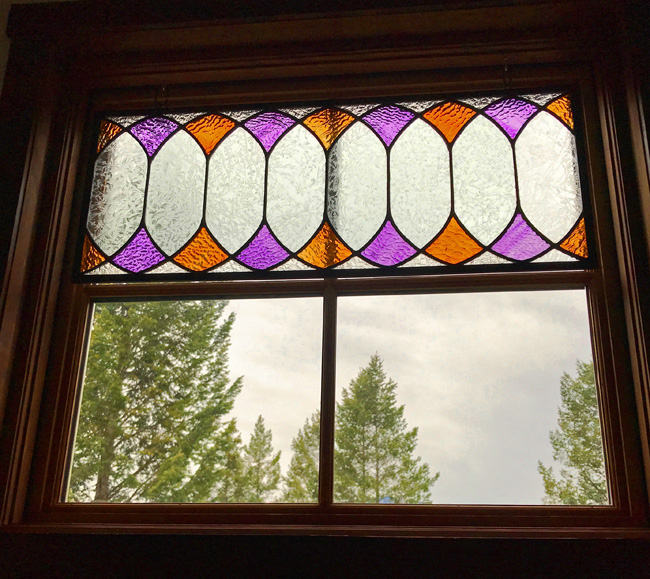A square window features a band of purple and gold stained glass across the top