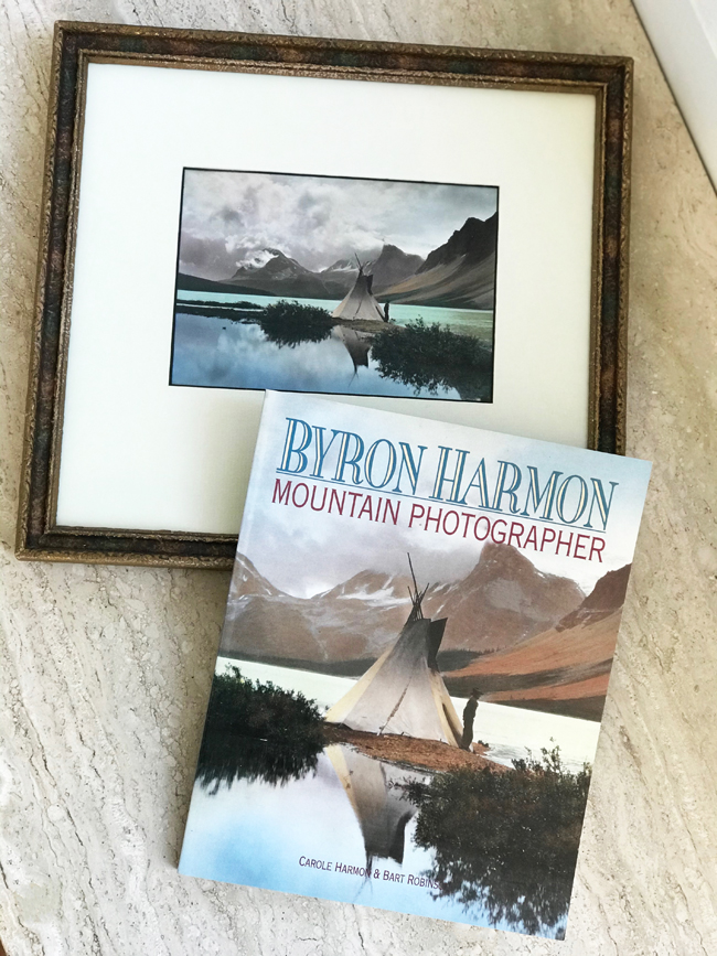 Framed photo of tent beside a lake, mirrored by the book beside it featuring the photographs of Byron Harmon