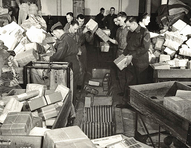 Men in Royal Canadian Air Force uniforms sort mountains of mail at postal depot during wartime