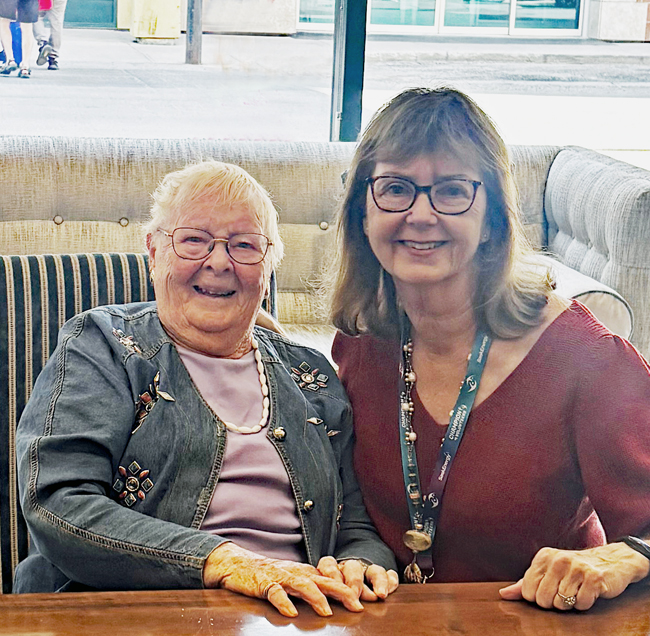 Elderly woman with white hair sits next to younger woman with long brown hair, both smiling at camera