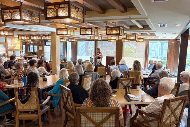 Woman standing at podium, speaking to a crowd of seated people